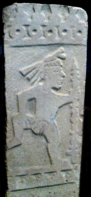 stone relief of dancing naked woman with leg raised, hoisting spear or staff